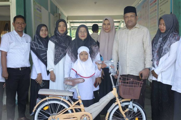 Alia Alia berdiri sembari memegang sepeda baru miliknya yang dihadiahkan oleh H. Mukhlis. Foto: ist.
