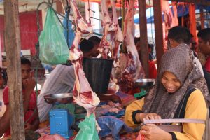 Seorang ibu tersenyum sembari mengambil uang di dompet ketika hendak membayar daging makmeugang yang ia beli di pasar daging dadakan di terminal Matangglumpangdua, Bireuen(1/5/2022). Foto:Komparatif.id/Riski Aulia Ramadhan. 