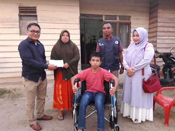 Sandi menyerahkan santunan dari Dr. Safrizal untuk Anwar. Kursi roda bantuan dari Kasat Reskrim Pidie Jaya Iptu Dedy Mizwar diharapkan dapat memudahkan Anwar dalam beraktivitas. Foto: Komparatif.id/Muhajir Juli.
