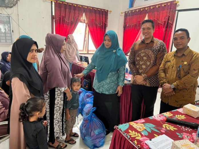 PKK Aceh Utara Nibong cegah stunting, Pj Ketua PKK Nurmaziah, SE.Ak, M.Si saat menyerahkan bantuan PMT untuk bayi dan balita di Aula Puskesmas Nibong, Jumat (24/6/2023). Foto: Komparatif.ID/Fuad Saputra.