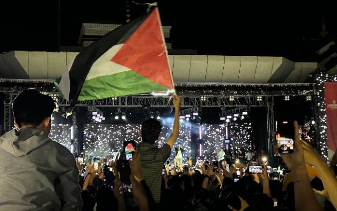 Andika Kangen Band Guncang Panggung Bhayangkara Fest 2024 Penonton mengibarkan bendera Palestina saat menonton penampilan Andika Kangen Band pada Bhayangkara Festival 2024 di Taman Sultanah Safiatuddin, Banda Aceh, Sabtu (7/7/2024). Foto: Komparatif.ID/Fuad Saputra.