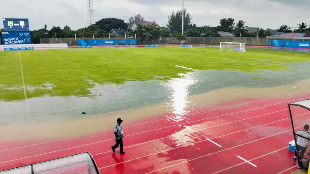 Tergenang Air Hujan, Laga Papua vs Riau Terhenti 45 Menit Sepakbola PON 2024: Papua Kalahkan Riau 1-0 Stadion Blang Paseh, Kota Sigli, Kabupaten Pidie tergenang air hujan cukup parah sehingga menyebabkan laga Papua vs Riau pada Senin (2/9/2024) harus dihentikan sementara. Foto: Komparatif.ID/Harmadi.